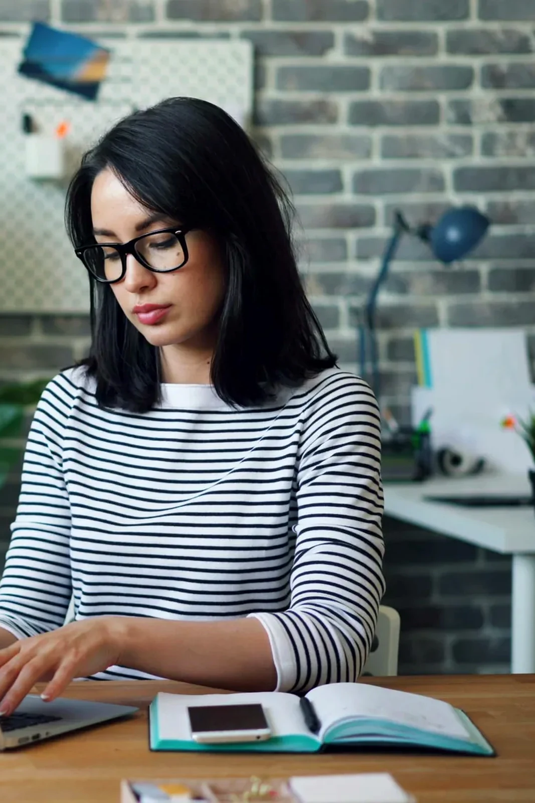 Freelancer focused on typing from a polished studio workspace with glasses and notebook nearby.